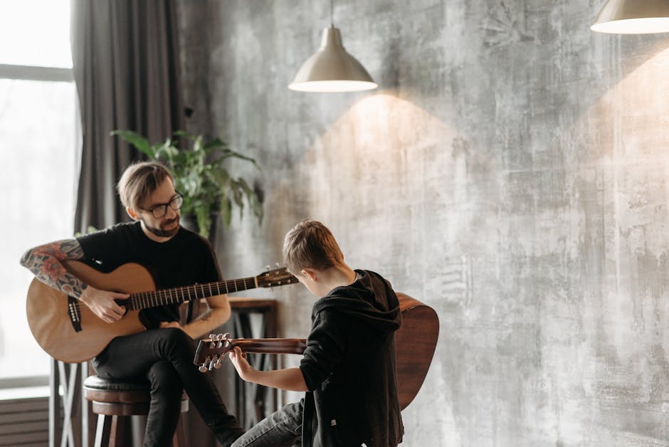A man and a boy engaged in a guitar lesson, playing acoustic guitars indoors.